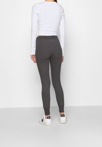 Grå leggings i mjukt material med en åtsittande design, kombinerade med en vit ribbad långärmad topp och vita sneakers med svarta accenter.