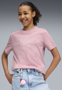 T-shirt en coton rose à manches courtes avec un logo "Puma" brodé en blanc. Associé à un short en denim taille haute et un porte-clé à pompon.