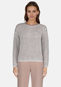 Lekki, srebrny sweter dzianinowy o luźnym, otwartym wzorze, okrągłym dekolcie i długich rękawach; w zestawie z beżowymi spodniami.