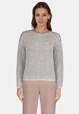 Lekki, srebrny sweter dzianinowy o luźnym, otwartym wzorze, okrągłym dekolcie i długich rękawach; w zestawie z beżowymi spodniami.