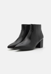 Botas de cuero negras hasta el tobillo con punta afilada, tacón medio y una textura suave. Cuentan con una cremallera lateral para facilitar su uso.