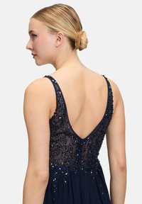 Granatowa wieczorowa suknia z głębokim dekoltem na plecach, ozdobiona misterną niebieską koronką na przezroczystej górze i zwiewnym trenie.