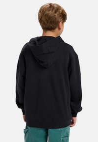 Čierna mikina s kapucňou vyrobená z mäkkého materiálu, s veľkou kapucňou a rebrovanými manžetami. Na zadnej strane má jednoduchý dizajn bez grafiky.