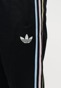 Mustad spordipüksid pastelse sinise, roosa ja kollase vertikaalse triibuga ning valge Adidas trefoil logo tasku lähedal.