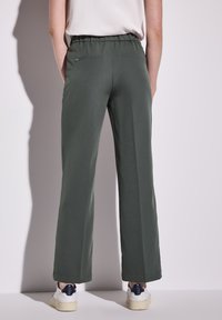 Pantalons larges verts avec une taille élastique, deux poches arrière et une texture de tissu lisse, associés à des baskets blanches.
