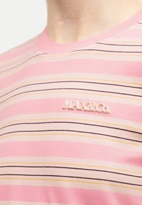 Κοντινό πλάνο ενός ριγέ πουκαμίσου σε ροζ και μπεζ με το λογότυπο "MAX&Co." κεντημένο στο στήθος.