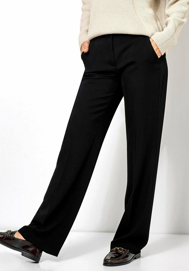 Black wide-leg trousers made of smooth fabric. Features two side pockets and a tailored waistline. Paired with brown loafers.