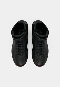 Černé kožené vysoké boty s kulatou špičkou, kontrastním prošíváním a šněrováním. Vnitřek zdobí viditelné logo.