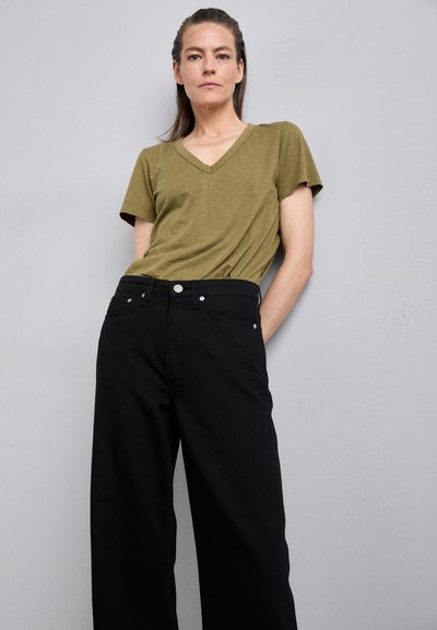 Olive green v-neck t-shirt paired with high-waisted black wide-leg trousers, featuring metal button and pocket details. Matte fabric texture.