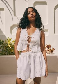 Witte linnen crop top met bloemenborduursel en gegolfde randen, gecombineerd met bijpassende witte shorts met een elastische tailleband en zakken.
