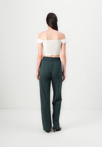 Haut blanc à épaules dénudées avec des manches volantées, associé à un pantalon ample vert foncé. Le pantalon présente une taille élastique et des jambes droites.