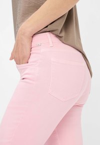 Jeans rosa aderenti in denim, con un classico design a cinque tasche e un piccolo logo sul retro della vita.