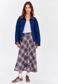 Džínová bunda s hnědým koženým límcem, kostkovaná sukně v modrých a hnědých odstínech a hnědé tenisky s bílými detaily; styl s vrstvením.