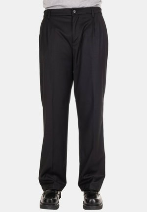 Pantaloni sartoriali neri indossati con scarpe di pelle nere e una camicia grigia chiaro infilata, mostrati dalla vita ai piedi.