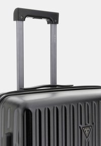 Valigia rigida nera con righe verticali, dotata di una maniglia nera e di un trolley retrattile grigio. Include un accento del logo vicino alla base.