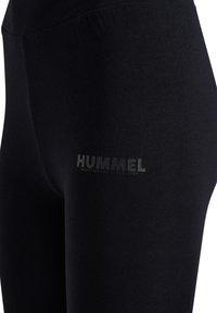 Nahaufnahme von schwarzen Sportleggings mit reflektierendem „HUMMEL SPORTSWEAR SINCE 1923“-Logo am oberen Oberschenkel.