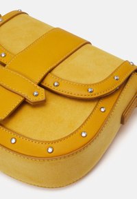Borsa gialla in pelle liscia e morbida suede, con borchie decorative in argento e un audace design della tracolla.