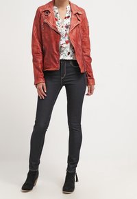 Red leather motorcycle jacket with textured finish, floral blouse, dark skinny jeans, and black ankle boots with tassels.