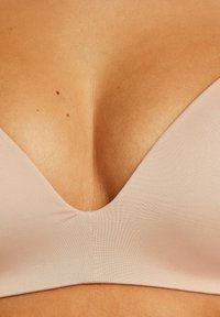 Reggiseno in tessuto leggero e liscio di colore nudo con un design a scollatura profonda a V. Presenta coppe senza cuciture e dettagli di texture delicati sui bordi.