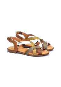 Sandali in pelle marrone con fasce intrecciate multicolori in verde, oliva e bianco. Suola piatta con cinturino alla caviglia regolabile.