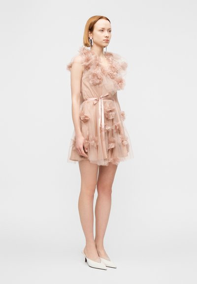 Ρόζ τούλινο φόρεμα με διακοσμητικές εφαρμογές λουλουδιών, μέση με κορδέλα και φουσκωτή φούστα. Συνοδεύεται από λευκές μυτερές γόβες.