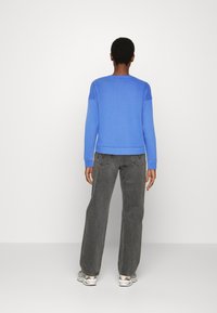 Sudadera azul de manga larga, con cuello y puños acanalados. Combinada con pantalones oscuros de corte ancho y deportivas con estampado. Diseño simple y casual.