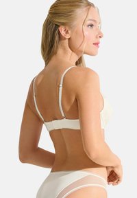 Witte lingerieset met een zacht gestructureerde beha met verstelbare bandjes en haak-en-oogsluiting. De slip heeft doorschijnende paneelaccenten.