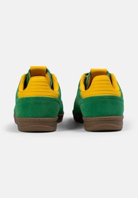 Zapatillas de ante verde con un collar y tab de talón acolchados en amarillo, suela de goma marrón y acentos texturizados en los laterales.