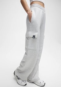 Graue Baumwoll-Sweatpants mit entspannter Passform, ausgestattet mit Seitentaschen und einer aufgesetzten Tasche am Oberschenkel. Der Bund ist elastisch.