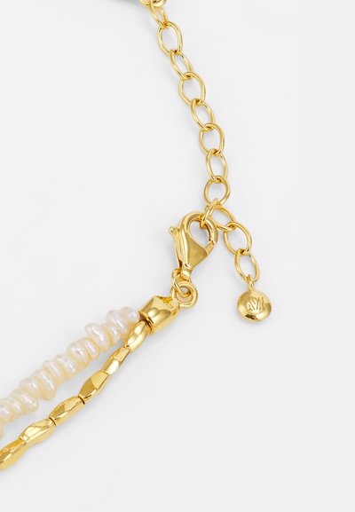 Collier en chaîne dorée ornée de perles blanches irrégulières et de maillons texturés, avec un fermoir à lobster et un petit détail en forme de charm rond.
