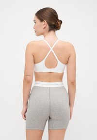Hvit Sports-BH med kryssrygg-stropper og nøkkelhullskutt, parret med grå shorts med snøring og en hvit elastisk midje.