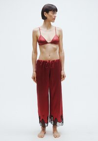 Czerwony satynowy komplet bielizny składający się z trójkątnego biustonosza i luźnych spodni ze ściągaczem, ozdobionych czarną koronką na dole.