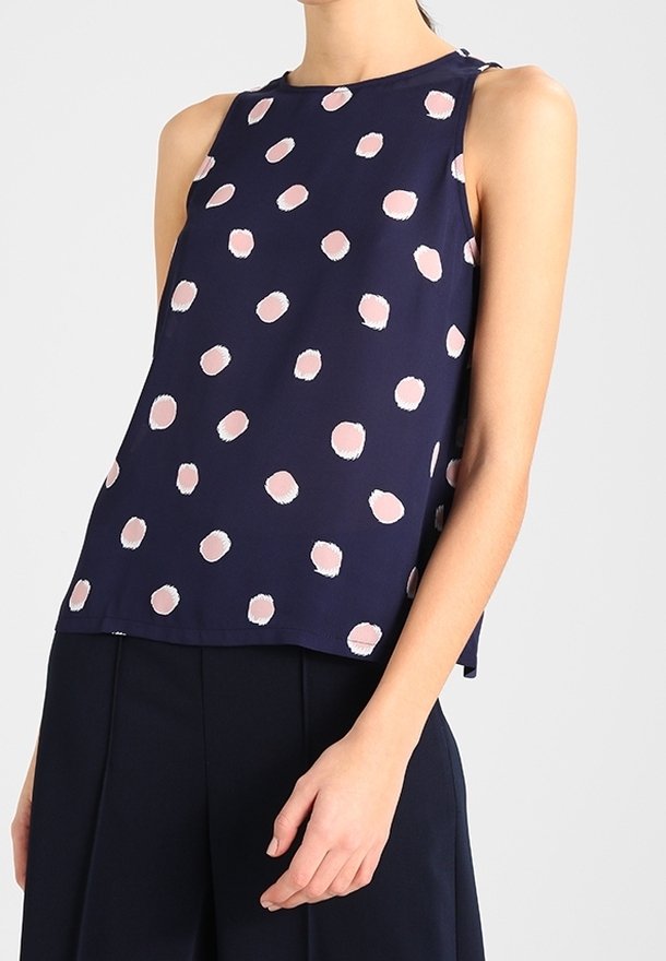 Haut bleu marine sans manches avec des pois rose clair irréguliers, porté avec un pantalon large bleu marine.