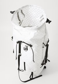 Rucsac alb cu textură, cu capac rulat, dotat cu curele negre, catarame și elemente din metal. Interiorul are un model în grilă. Logo-ul este afișat pe lateral.