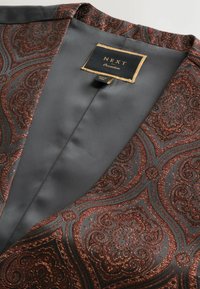 Schwarzes Satin-Kleidungsstück mit kupferfarbenem Paisleymuster; ausgestattet mit einem Etikett "NEXT Occasions". Glatte Textur, detaillierte Stickereien.