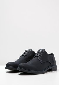 Des chaussures noires à lacets en tissu texturé avec une semelle extérieure lisse. Elles présentent un bout arrondi et des accents matériels minimalistes.