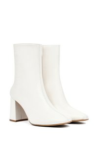 Bottes de cheville en cuir blanc avec des talons blocs, présentant un design épuré, une texture lisse et une pointe pointue. Détails de couture visibles.