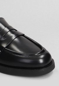 Mocassino in pelle nera con finitura liscia, punta rotonda e cinturino decorativo sulla parte anteriore. Suola in gomma con dettagli di cucitura discreti.