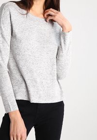 Jasnoszary sweter o fakturowanej powierzchni, z okrągłym dekoltem i długimi rękawami, charakteryzujący się luźnym krojem i subtelnym wzorem w drobne plamki.