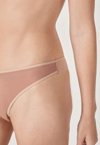Bas de bikini rose clair avec une finition lisse et texturée, présentant une ceinture sans couture et un design à couverture minimale.