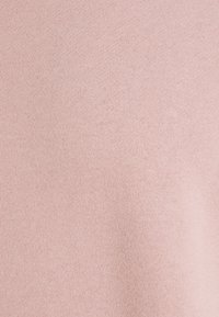 Texture de tissu tricoté rose pâle avec des points fins et réguliers, présentant un motif uniforme et une surface lisse.