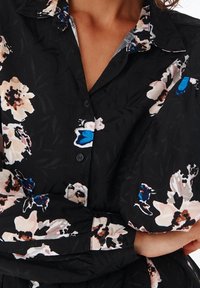 Černá květinová blůza s velkými světle růžovými a modrými květy, texturovaný materiál, límeček a zapínání na knoflíky vpředu.