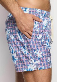 Costume da bagno da uomo con motivo floreale blu e bianco su sfondo geometrico rosa e viola, con vita regolabile con cordoncino e tasca laterale.