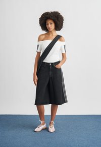 Μαύρα culottes από τζιν με λωρίδες στο πλάι, λευκό τοπ ώμου έξω και ροζ παπούτσια με κορδόνια. Ομαλή υφή και άνετη εφαρμογή.