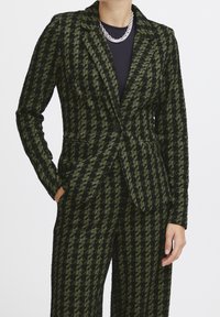 Blazer a quadri nero e verde con risvolti a incavo, chiusura con un bottone e due tasche frontali, realizzato in tessuto strutturato.