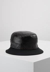 Pălărie neagră de tip bucket, cu un material lucios și texturat pe partea de sus, având o margine dintr-un material mat. Design simplu, rotund, fără modele sau accente suplimentare.