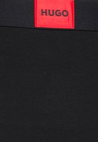 Black boxer briefs with a smooth texture and a wide elastic waistband featuring a red label with "HUGO" printed in black.