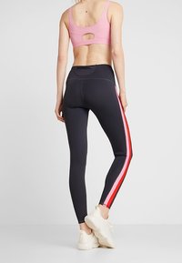 Leggings atletici neri con strisce laterali rosa e rosse, abbinati a un reggiseno sportivo rosa chiaro con un'apertura circolare sul retro.