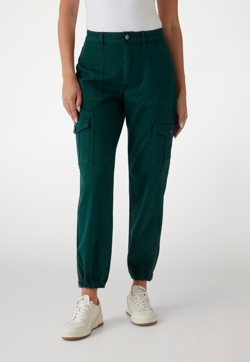 Zöldesszürke cargo nadrág, elasztikus mandzsettákkal, elülső és oldalsó zsebekkel, valamint testhezálló derékkal. Fehér sportcipővel párosítva az ellentét kedvéért.