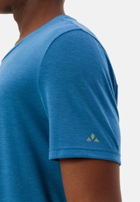 Blauwe kraagloze shirt met korte mouwen, gemaakt van gladde stof, met een V-hals ontwerp. Bevat een klein groen logo op de linker mouw.